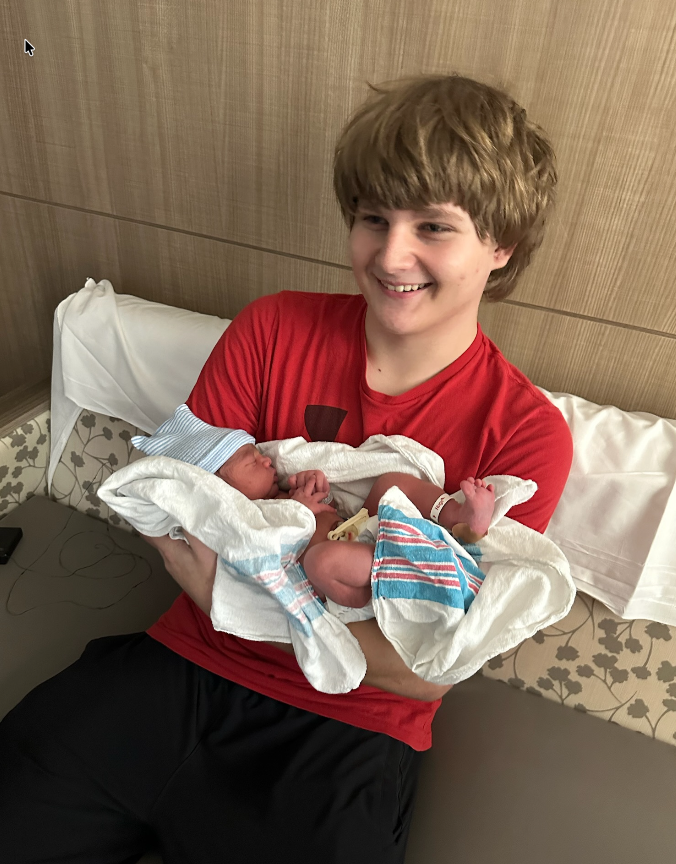 Trey smiling, holding a newborn in a hospital room.